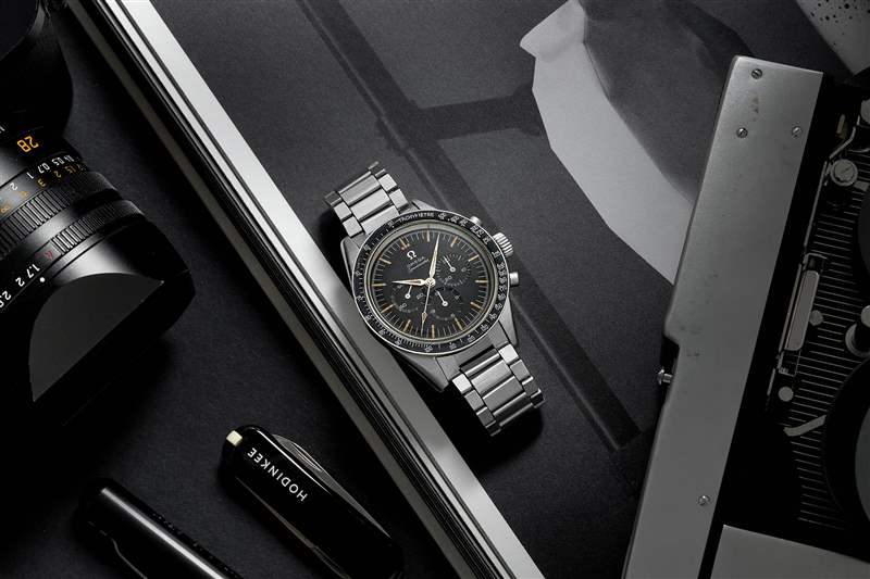 1960 年代 Omega Speedmaster Ref. 的生活方式圖片。 鋼手鏈上的 2998-6 旁邊是一本打開的書、一臺徠卡相機和一把黑色 HODINKEE 品牌的 Victorinox 瑞士軍刀。